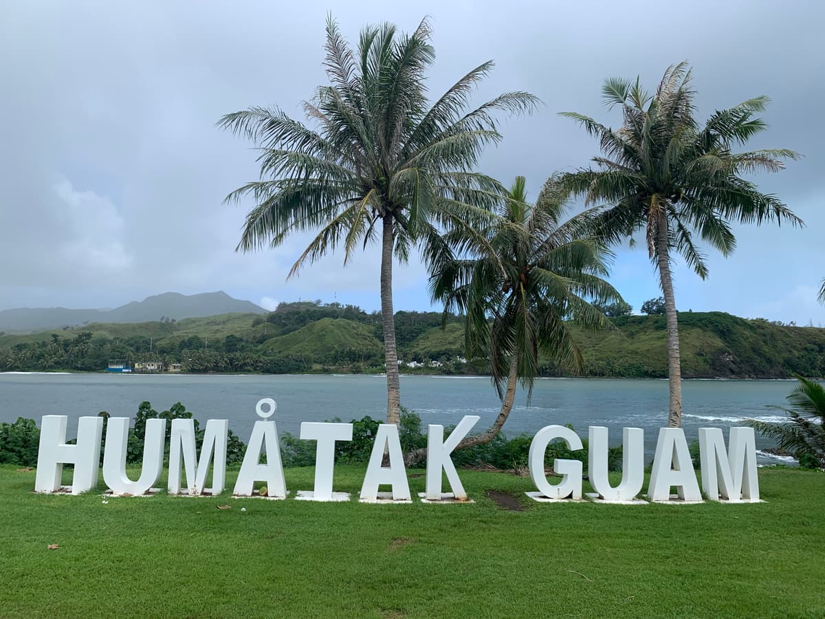 ヤシの木の前に並ぶHUMÅTAK GUAMの文字